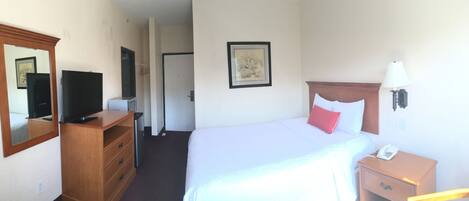 A hotel room with a bed, a bedside table with a lamp, a phone, a dresser, a TV, and a framed picture on the wall.