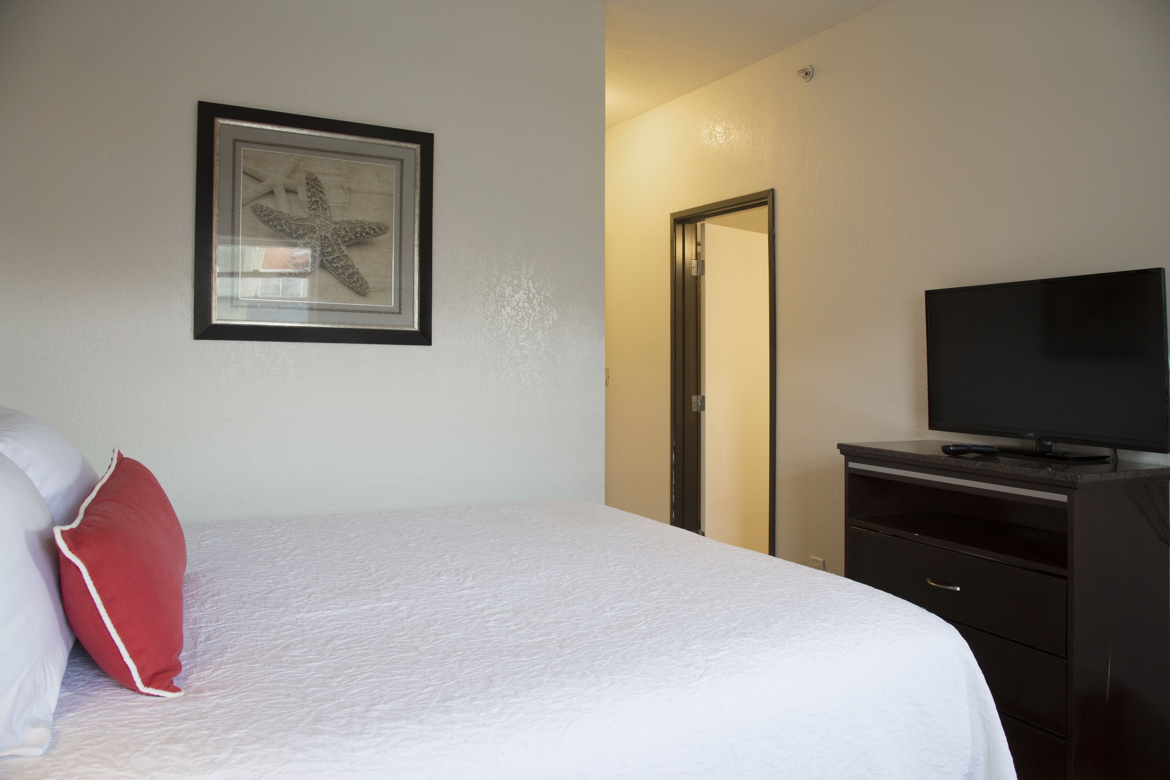 A hotel room with a bed, a television, a dresser, and a framed artwork on the wall.