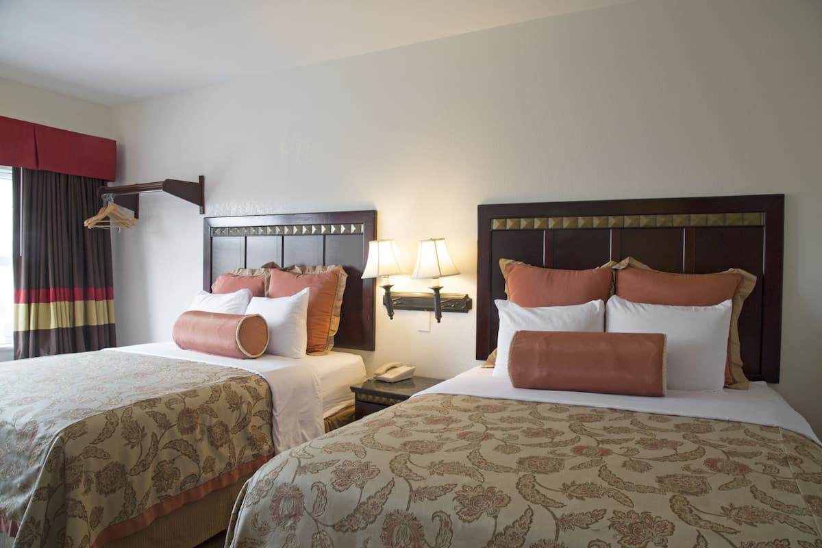 Habitación de hotel con dos camas, cada una con cabecero, lámparas de noche y teléfono en la mesita.