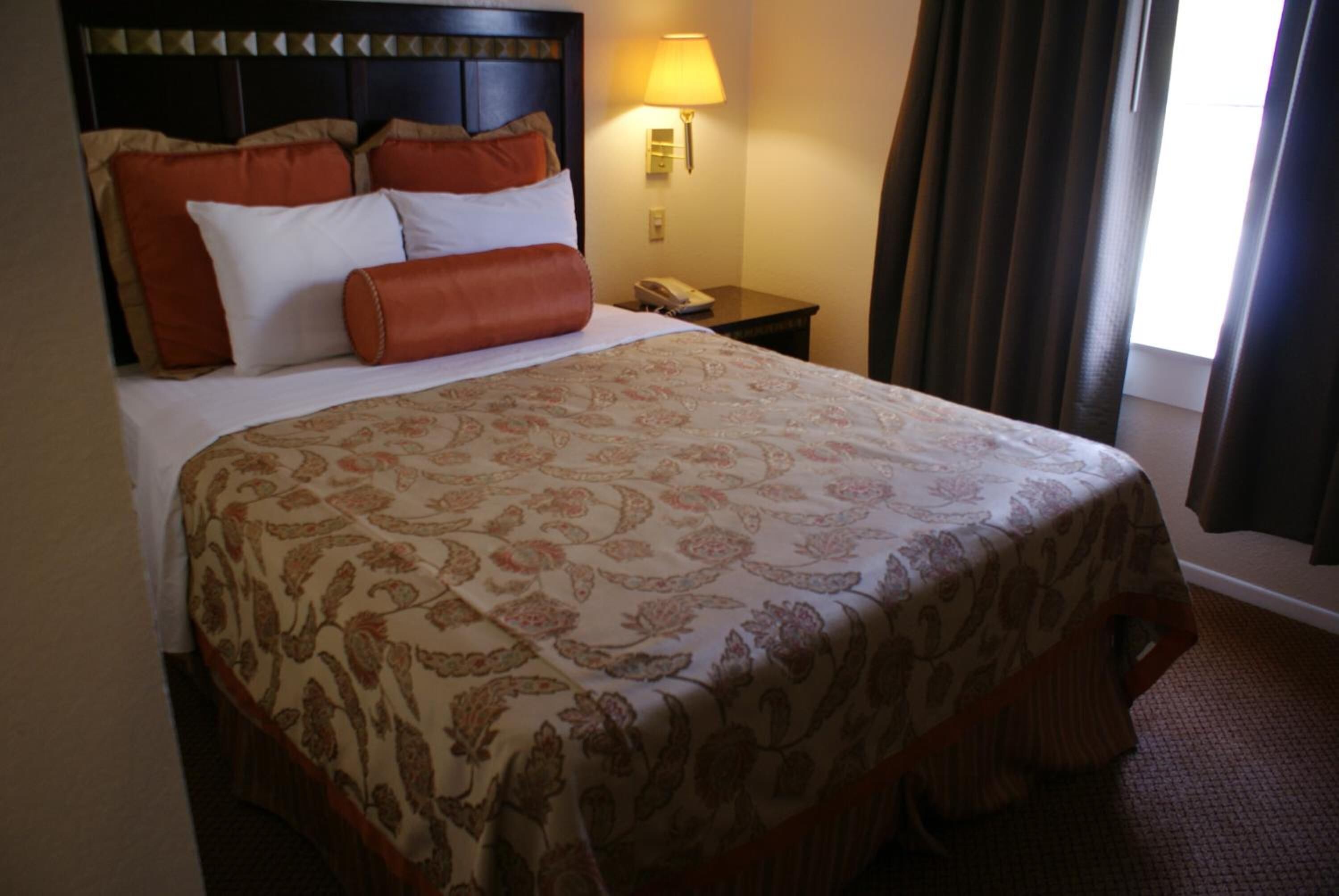 A hotel room with a large bed, a nightstand with a lamp, and a window with curtains.