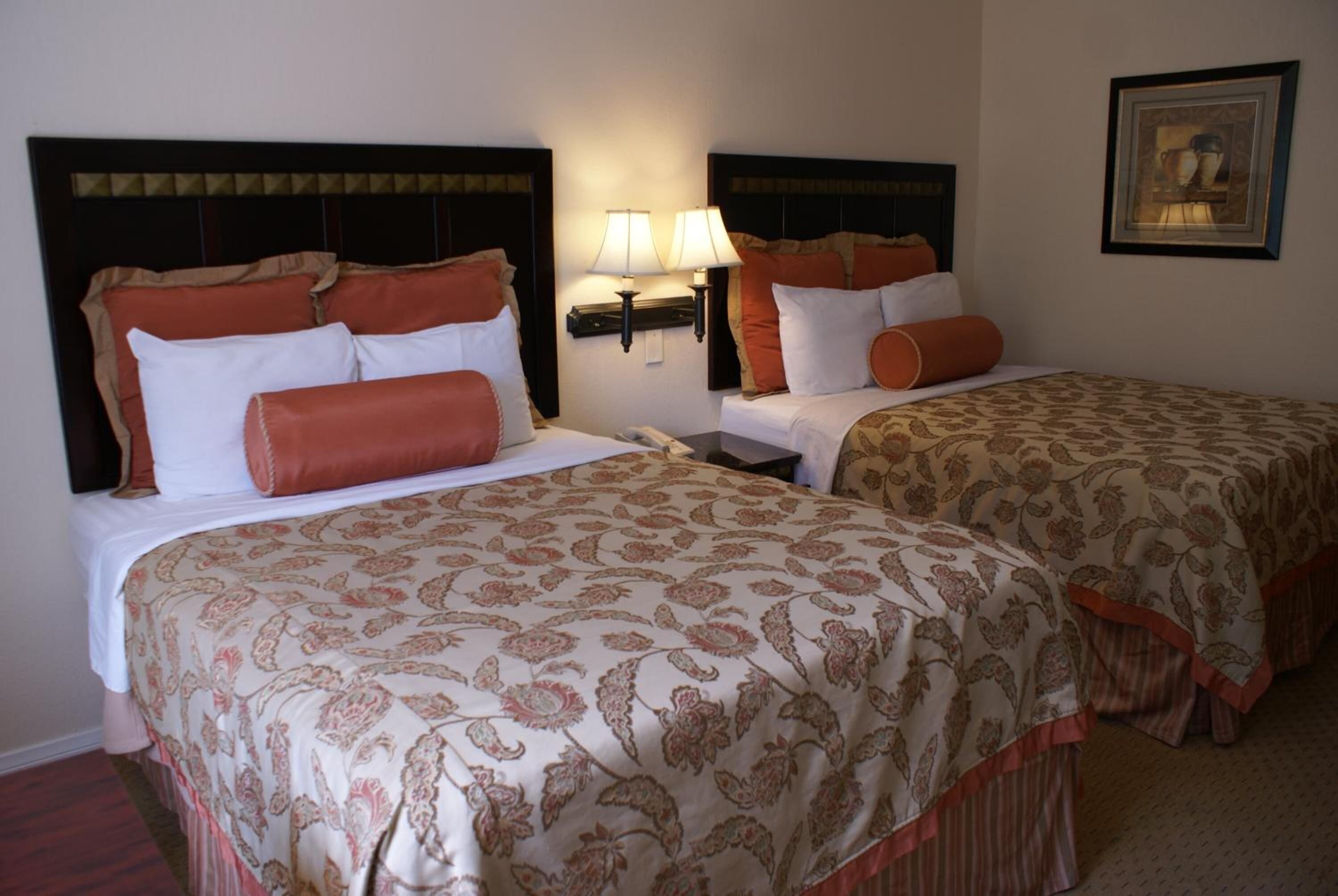 A hotel room with two beds, each with a headboard, a nightstand, and a lamp.