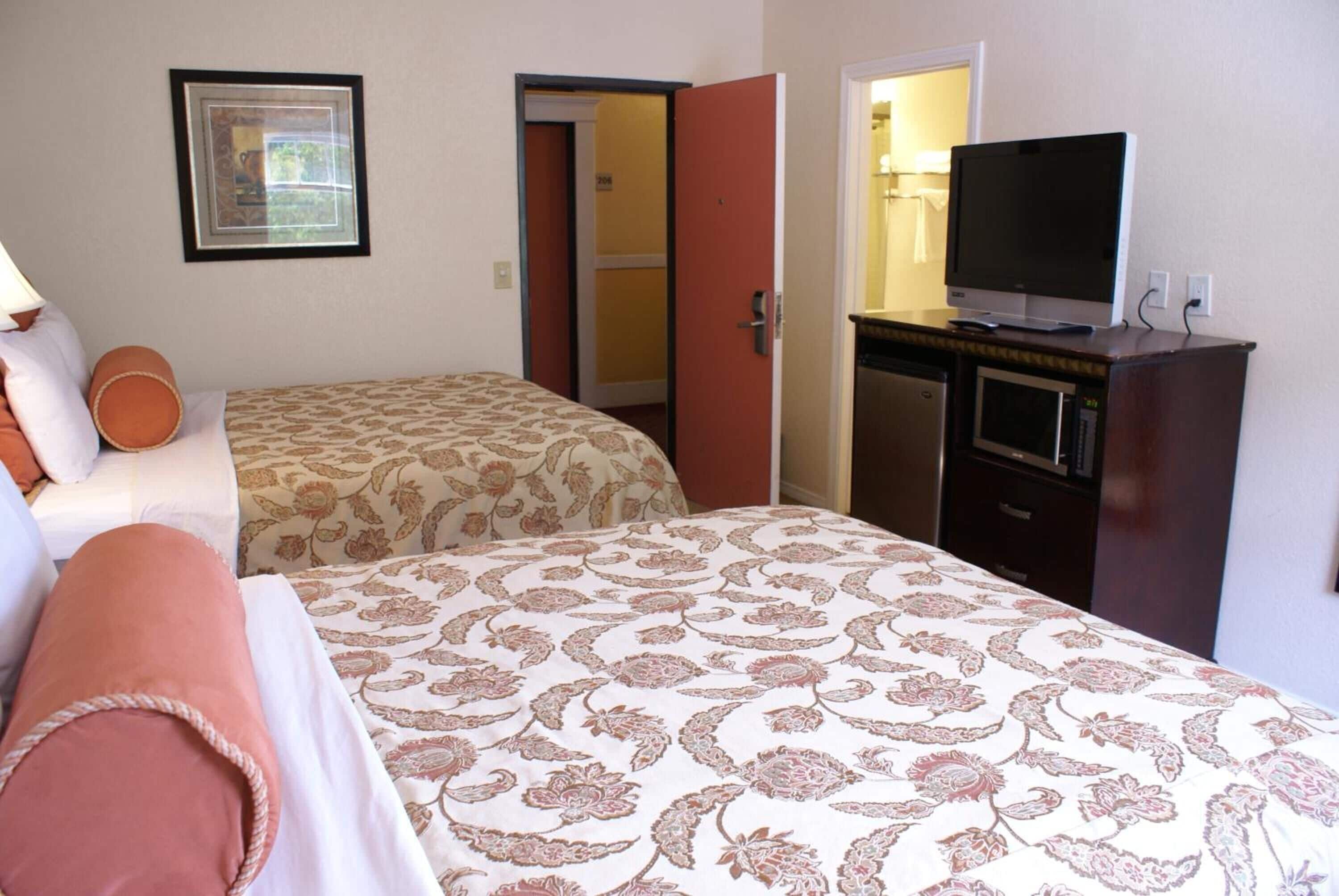 A hotel room with two beds, a television on a dresser, and a framed picture on the wall.