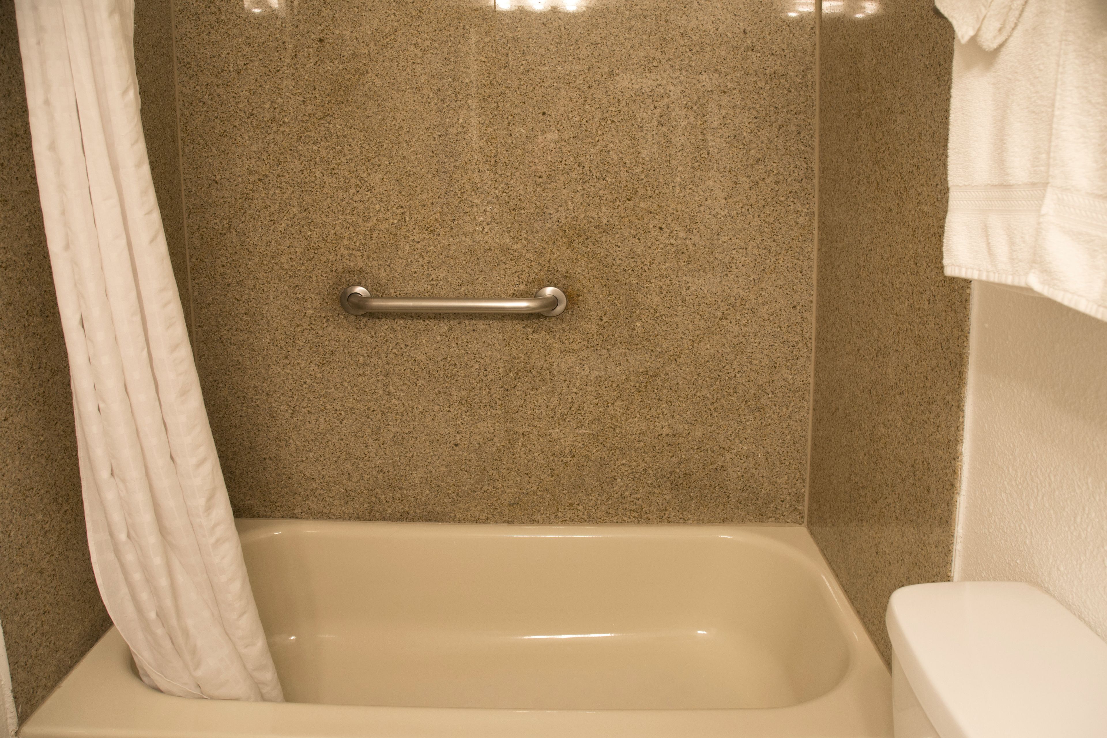 Un baño con bañera, ducha con barra de apoyo y un inodoro.