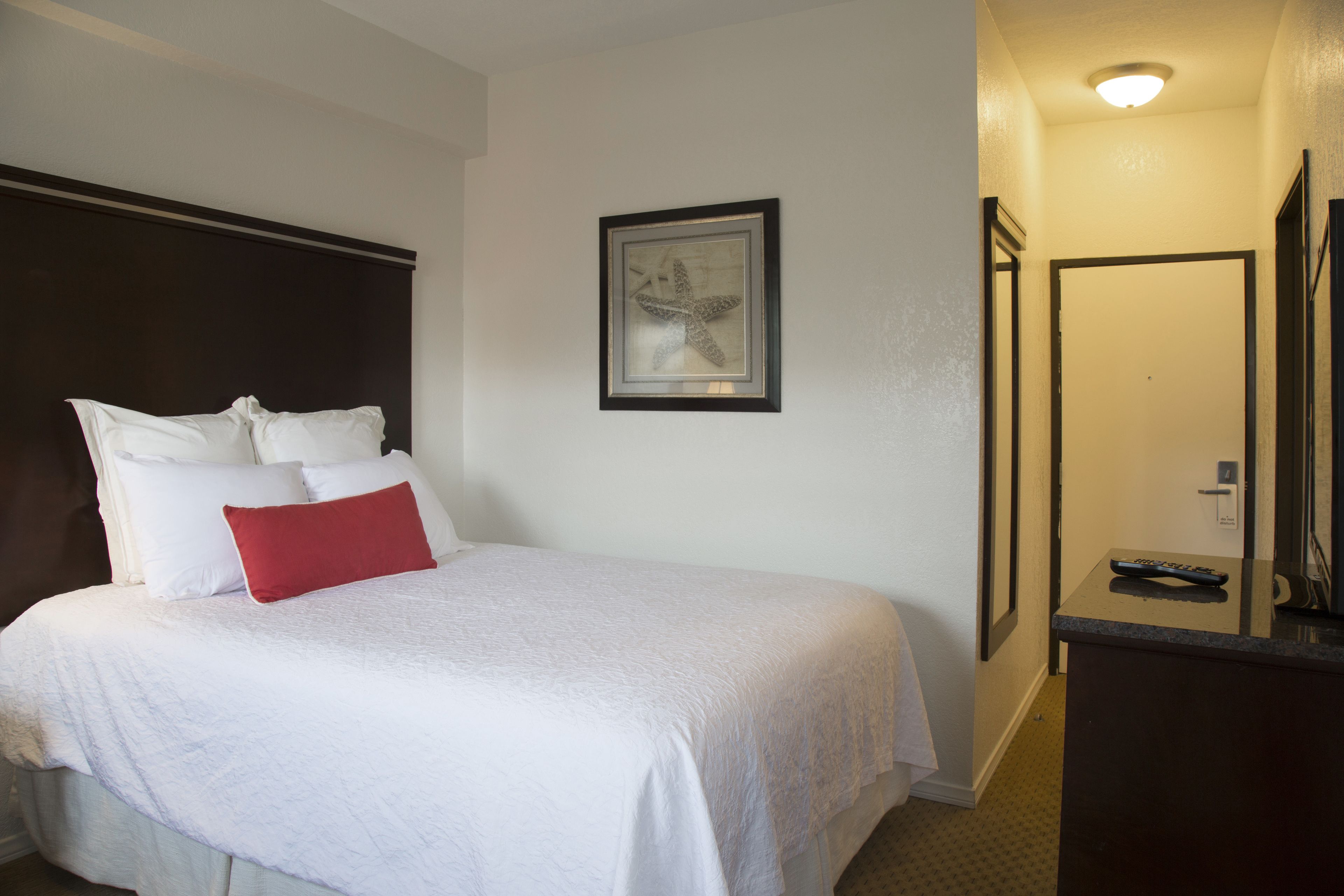 A hotel room with a bed, a framed artwork on the wall, and a door leading to a bathroom.