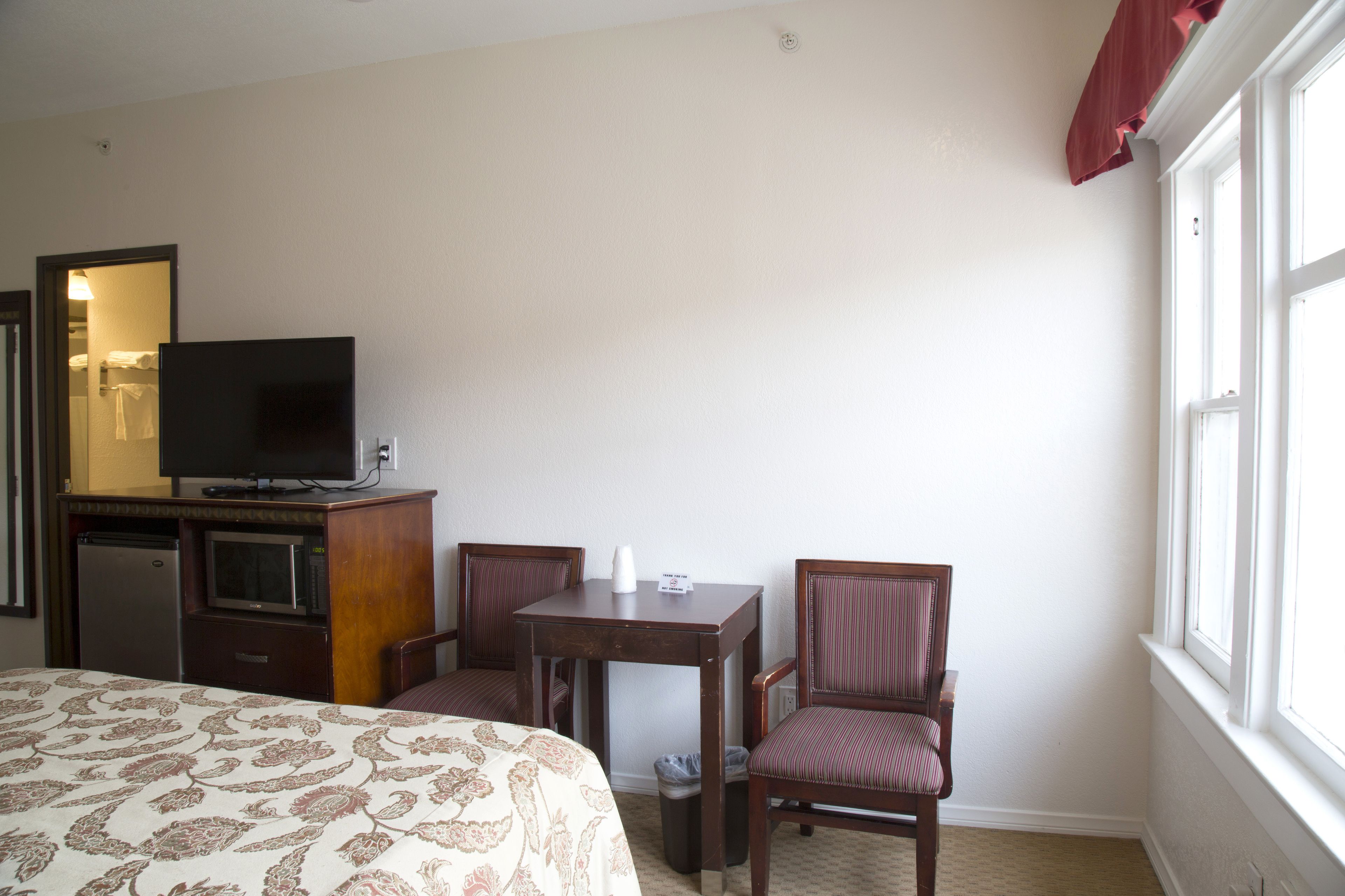 A hotel room with a bed, a desk with a chair, a television, and a window.