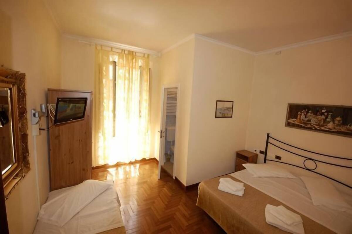 Hotellihuone, jossa on kaksi sänkyä, televisio, vaatekaappi ja taulu seinällä.