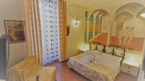 A hotel room with a bed, a nightstand, a chair, a curtain, and a wall with a painting. - Hotel Alexis (Rome)