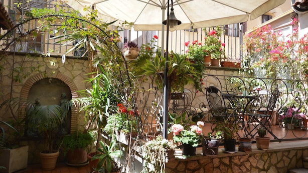 A covered outdoor area with potted plants and a metal table and chairs. - Hotel Alexis (Rome)