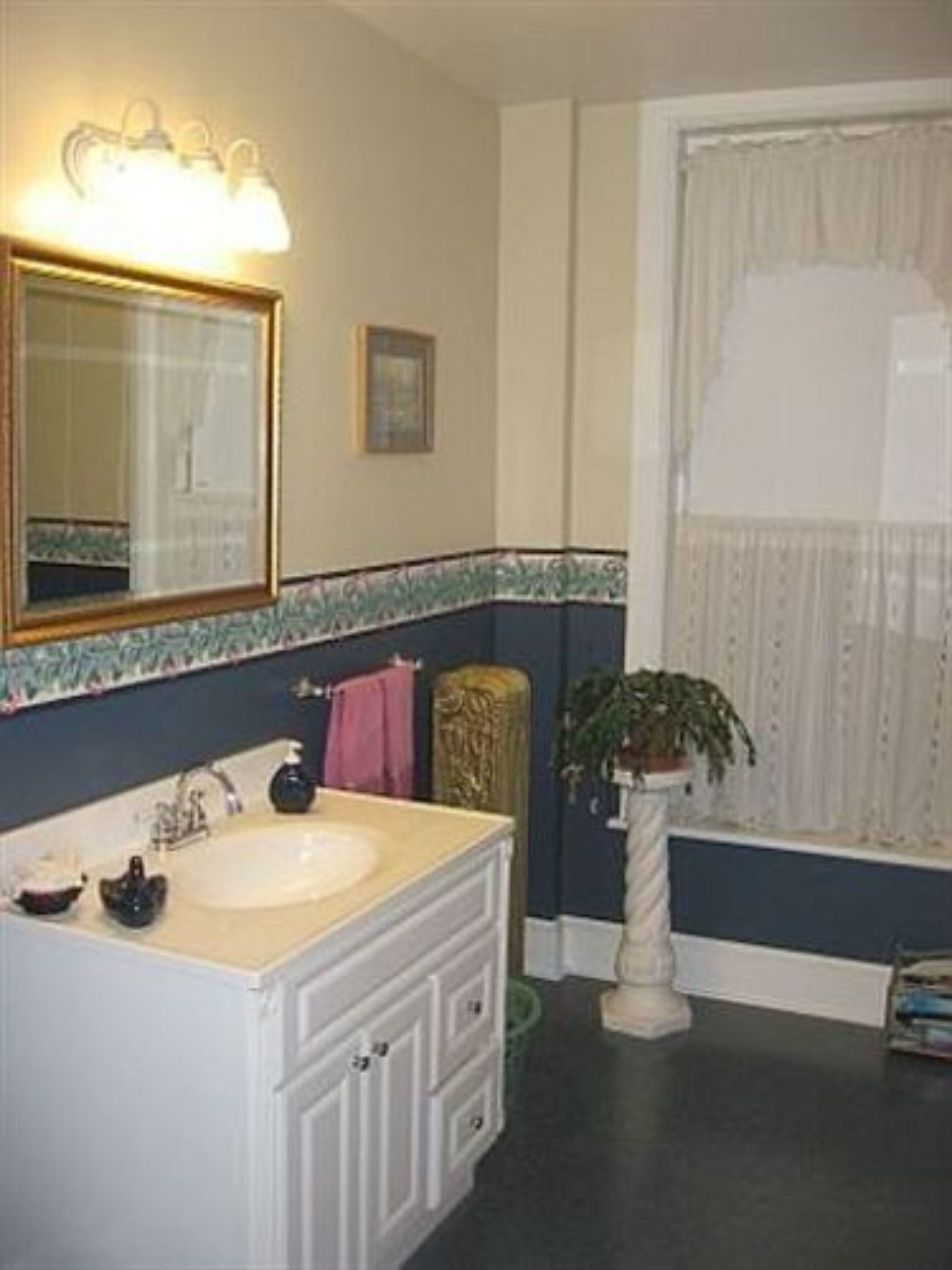 A bathroom with a large mirror, a sink, a vanity with drawers, a potted plant, and a window with curtains.