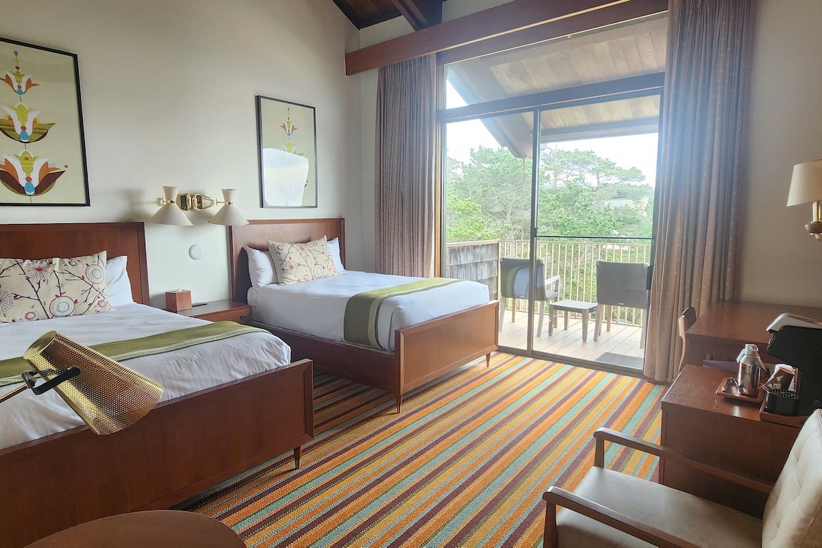 A hotel room with two beds, a balcony with a view, and a small seating area.