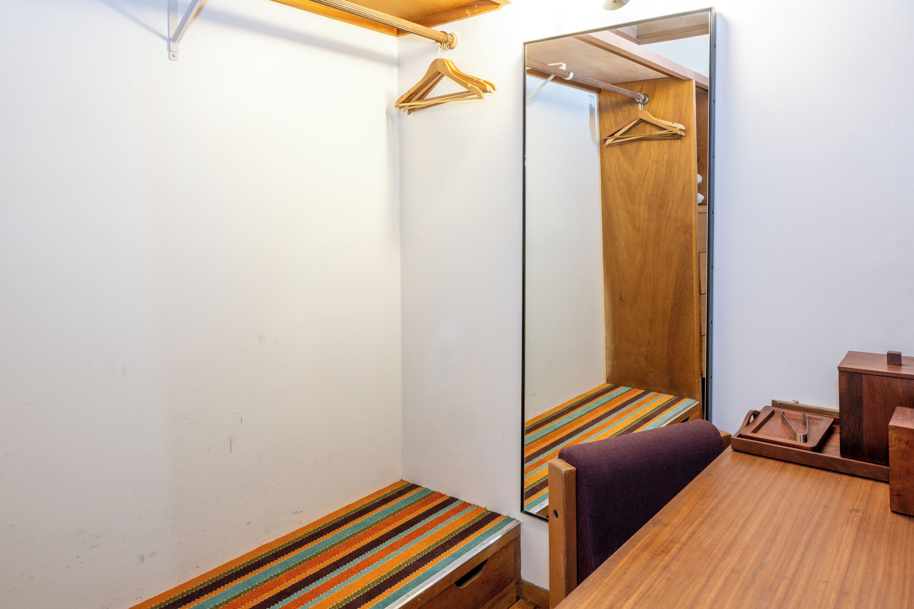 Een kleine kamer met een houten bankje, een spiegel en een houten kast.