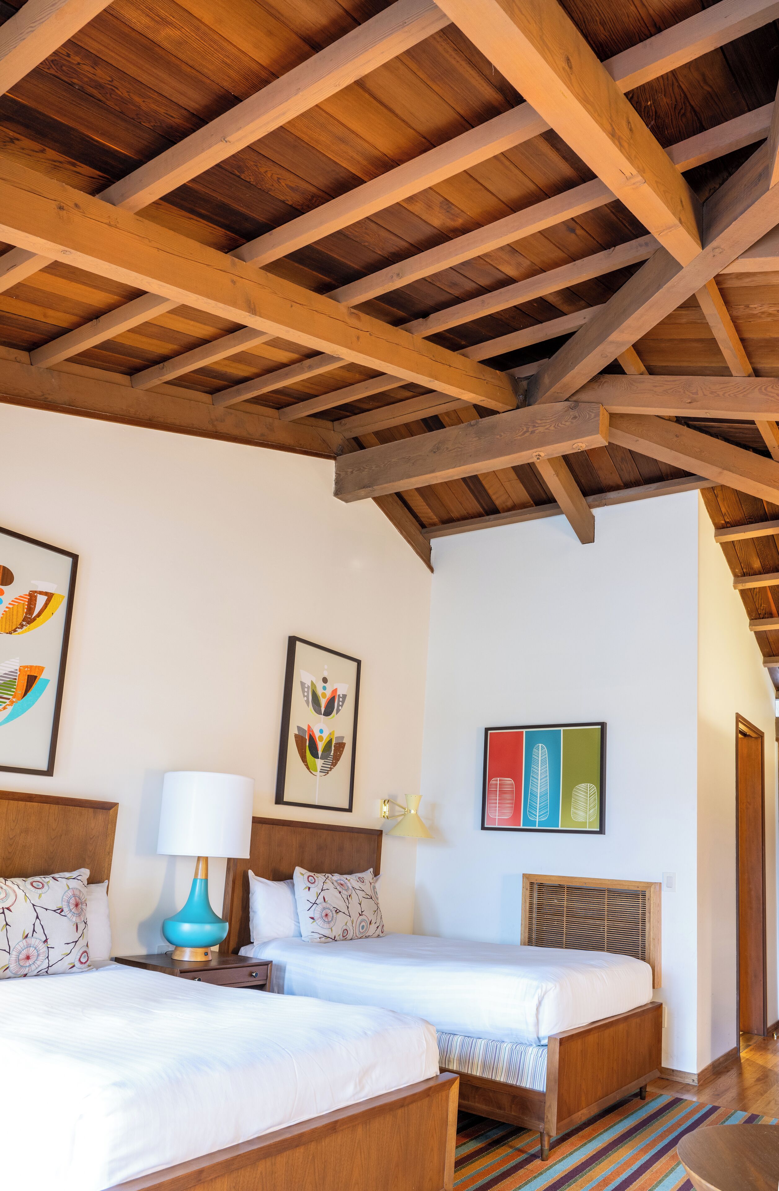 A room with two beds, wooden beams on the ceiling, and wall art.