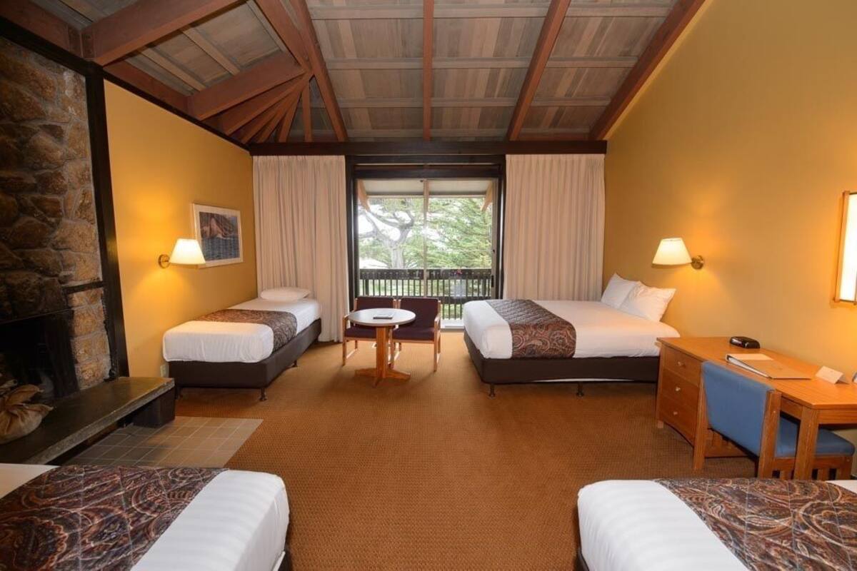 A hotel room with two single beds, a small table, a desk, and a fireplace.