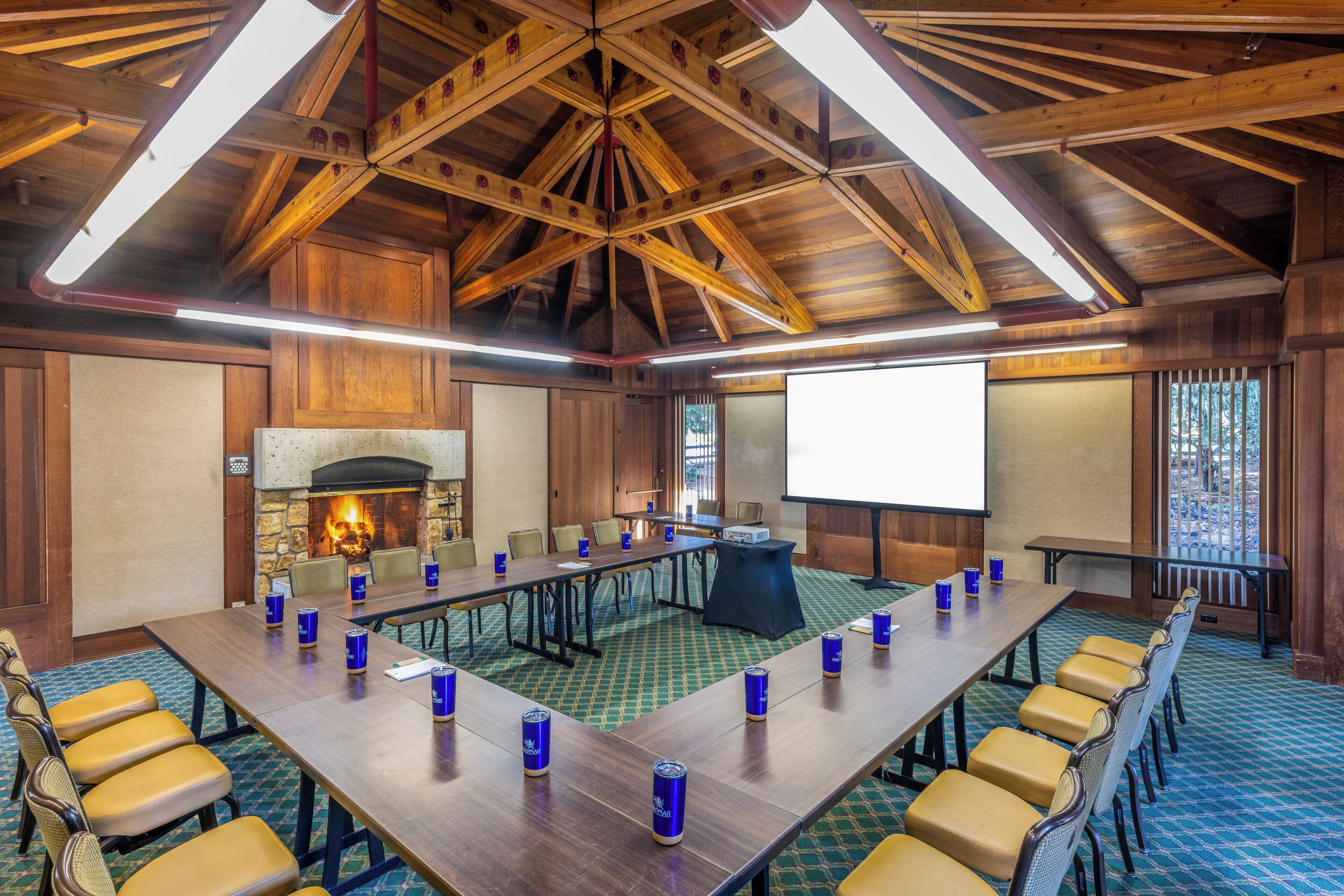 A conference room with a long table, chairs, a fireplace, and a projector screen.