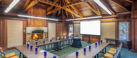 A conference room with a long table, chairs, a fireplace, and a projector screen.