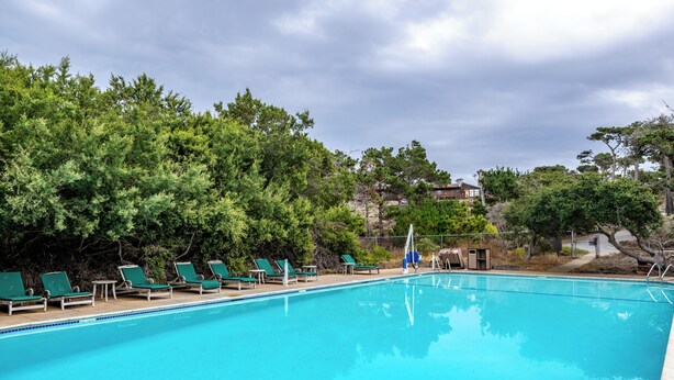 A swimming pool with green lounge chairs and a view of trees and buildings in the background.