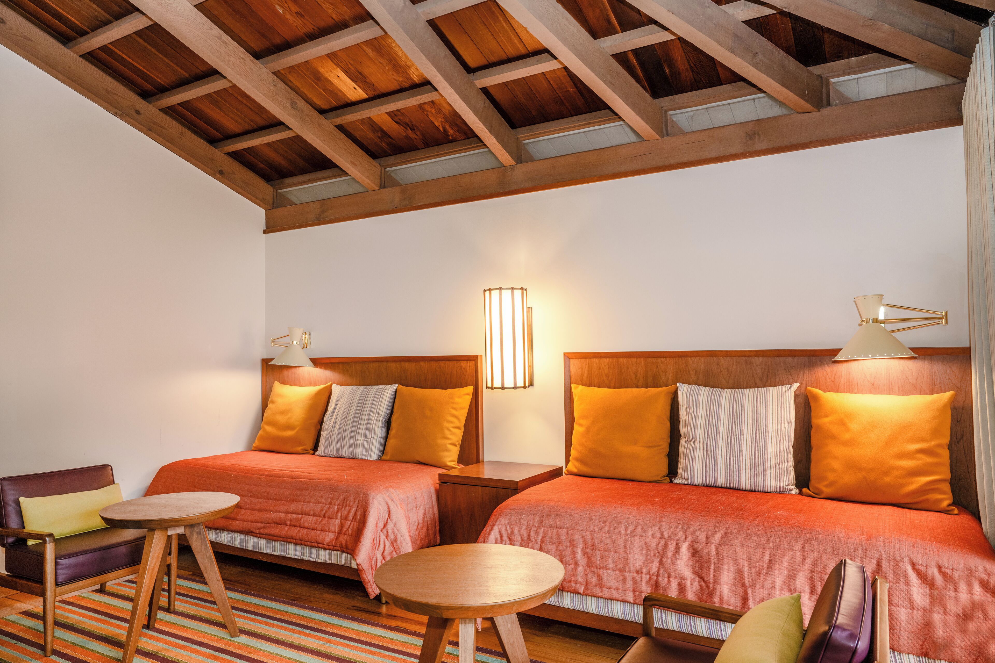 A hotel room with two beds, wooden headboards, a small round table, and a striped rug.