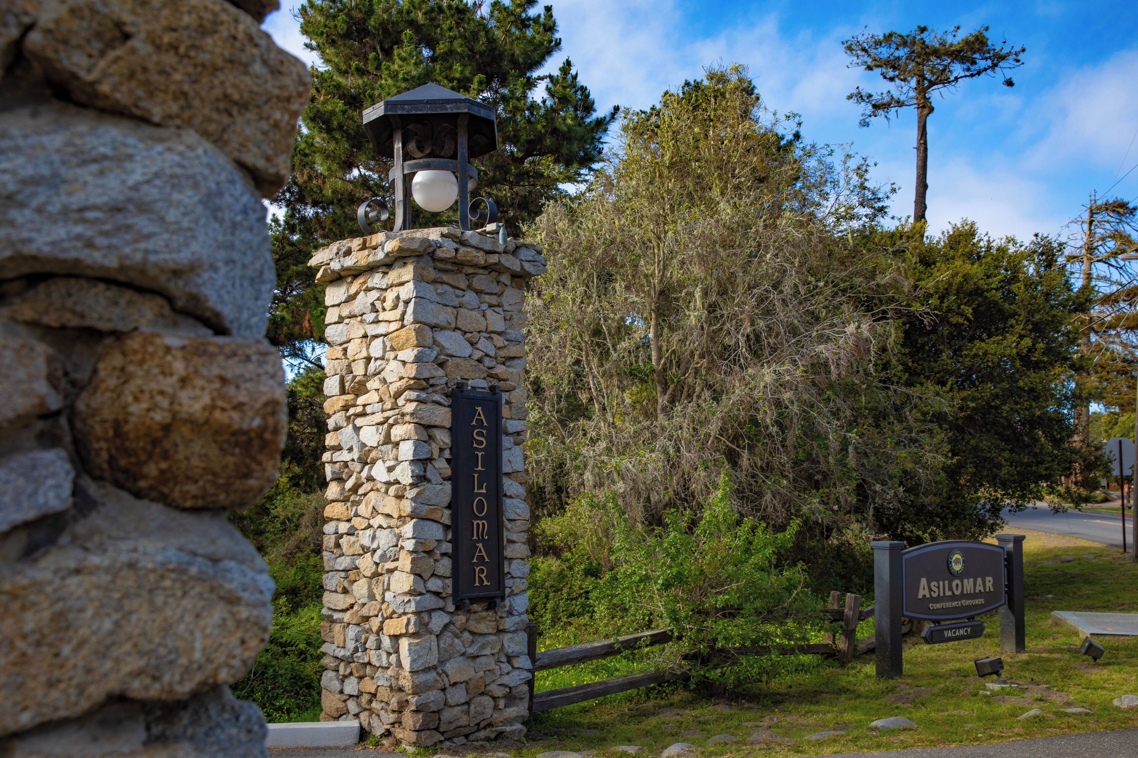 Eine steinerne Säule mit einem Schild, auf dem „Asilomar“ steht, und darunter ein kleineres Schild mit der Aufschrift „FREIE ZIMMER“.
