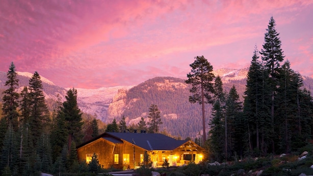 A lodge with a wooden exterior, surrounded by evergreen trees and snow-capped mountains.