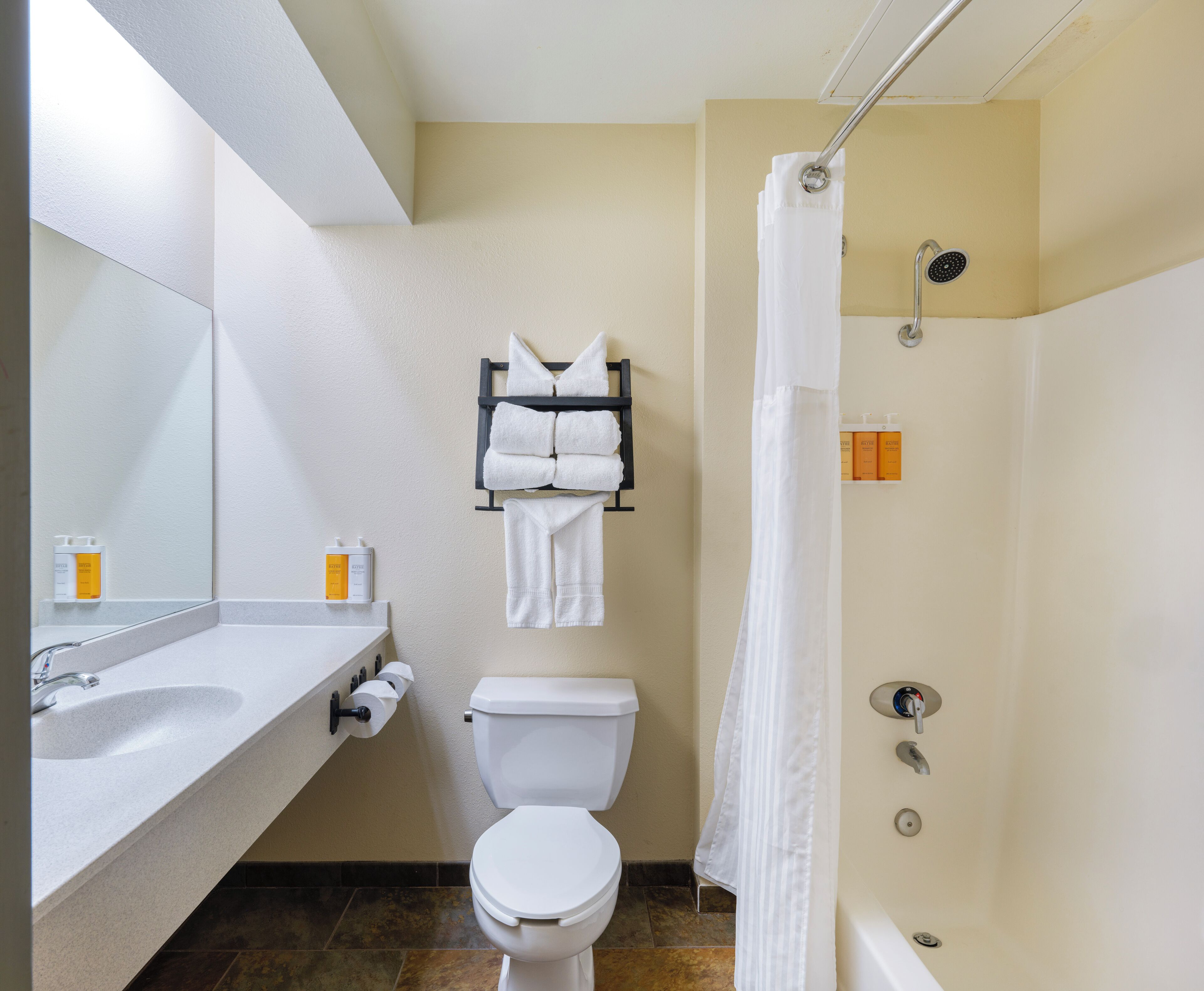 A bathroom with a sink, toilet, and shower. There are towels hanging on a rack and toiletries on the wall.