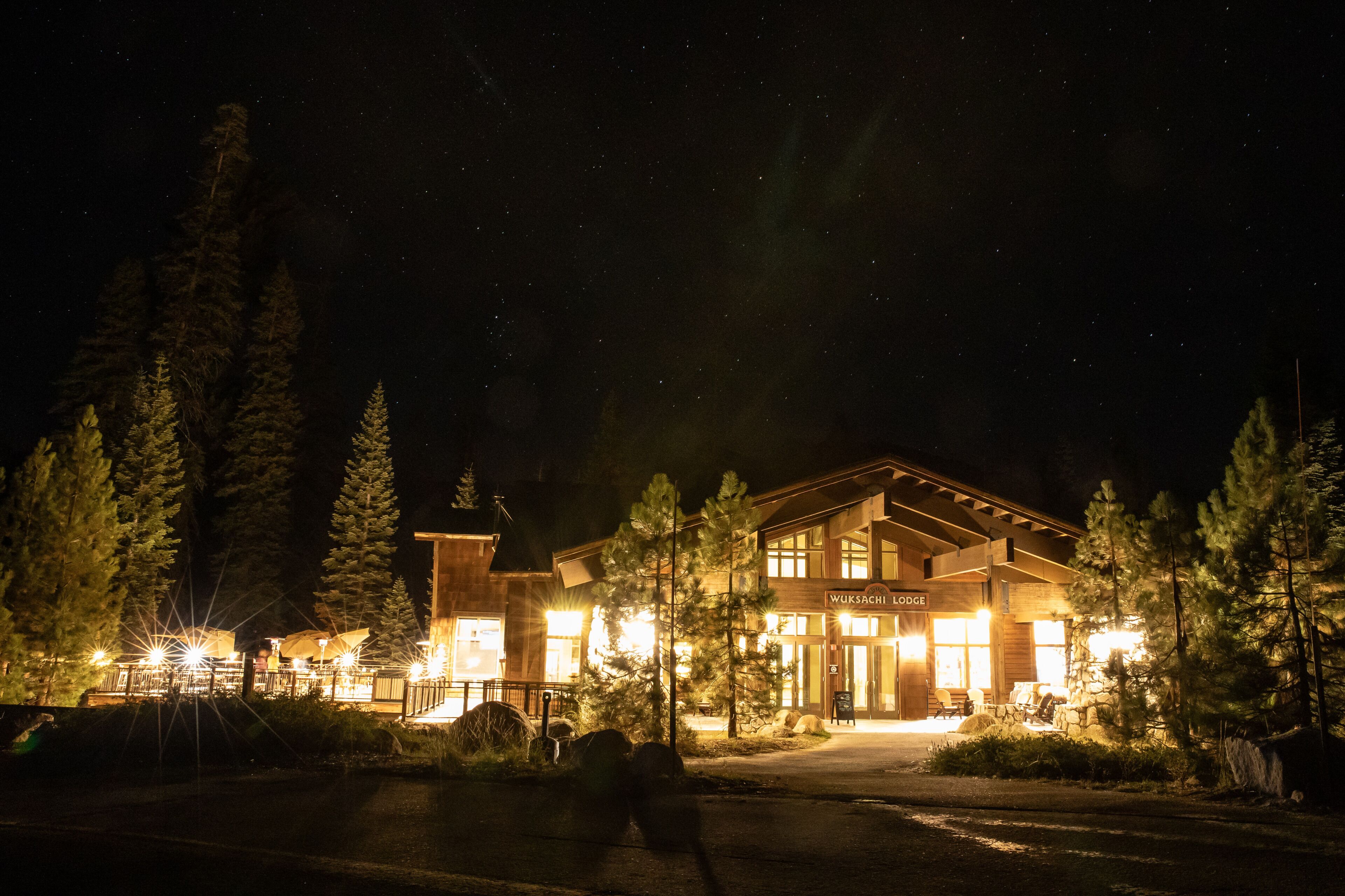 A lodge with a large entrance, surrounded by trees, and illuminated by exterior lights.