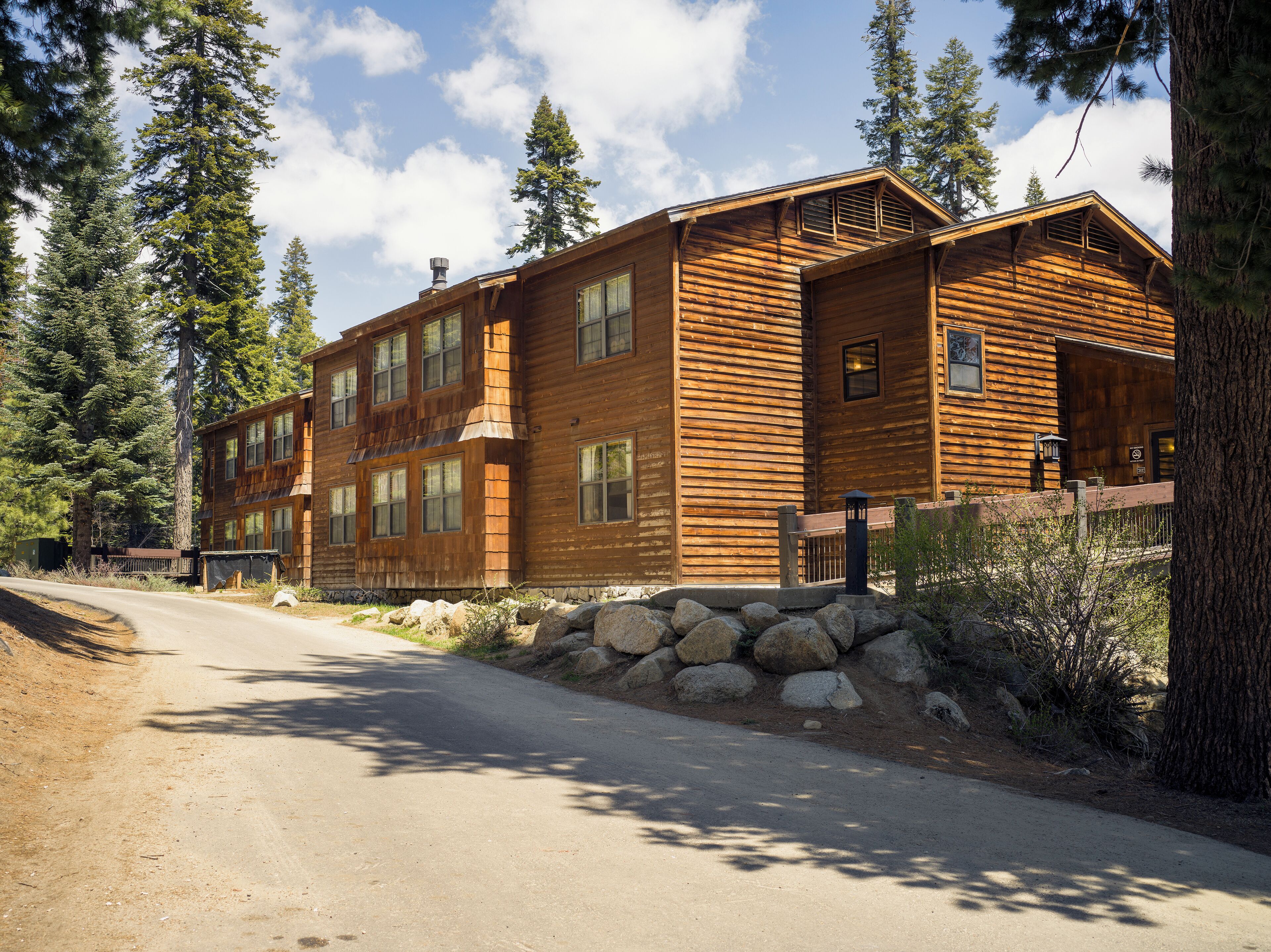 A two-story log cabin with a stone foundation, large windows, and a wooden deck.