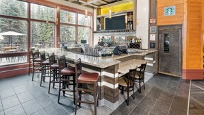 A modern bar area with a large island, bar stools, and a view of the outdoors.