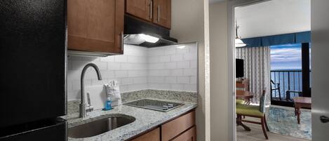 A compact kitchen with a sink, stove, and wooden cabinets. A dining area with a table and chairs is visible through an open door.