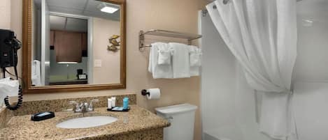 Ein Badezimmer mit einer Granit-Arbeitsplatte, einem Waschbecken, einer Toilette, einer Duschkabine mit Vorhang und einem Spiegel mit goldener Rahmung.