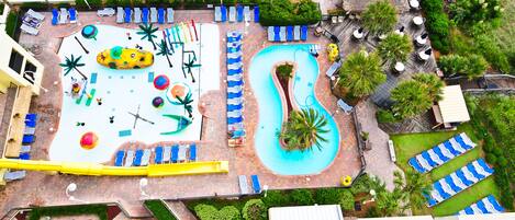 Luchtbeeld van een resort met een groot zwembad, meerdere loungegebieden met stoelen en parasols, en een glijbaan.