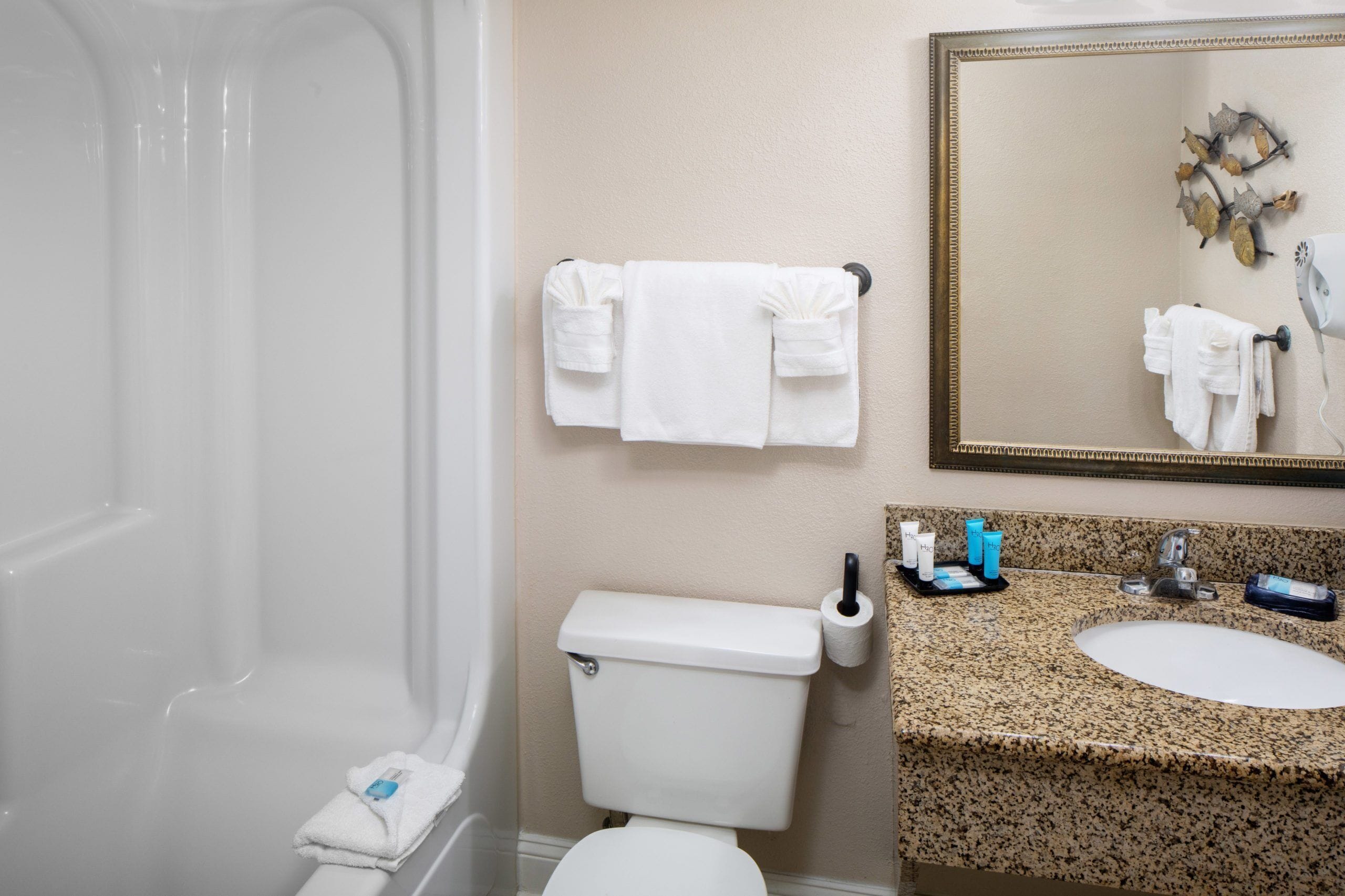 A bathroom with a bathtub, toilet, sink, and a mirror with a decorative leaf design.