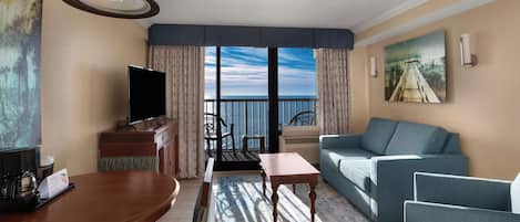 A hotel room with a balcony, a TV, a dining table, and a sofa.