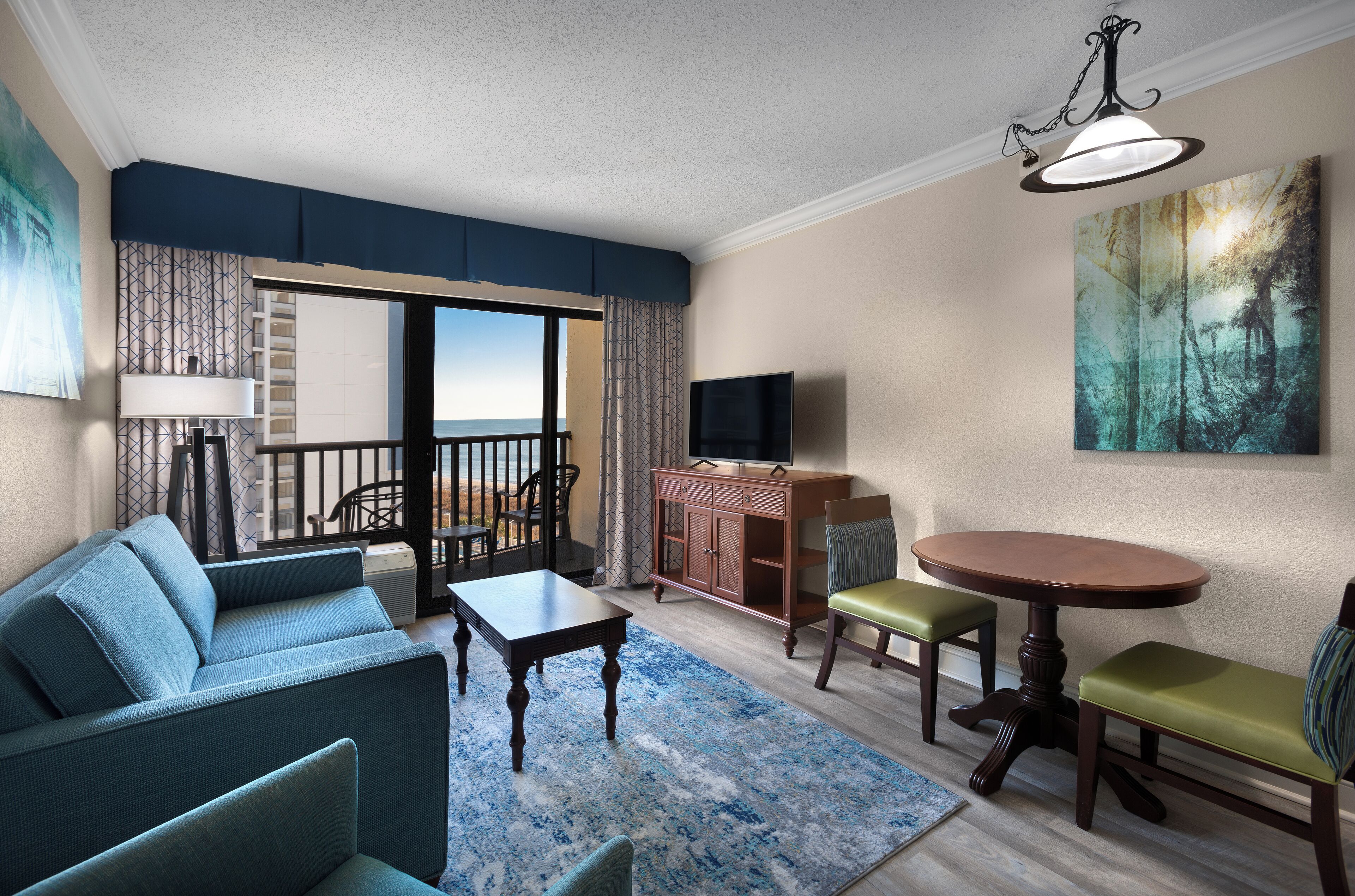 A living room with a sofa, coffee table, dining table, chairs, a TV, and a balcony with a view.