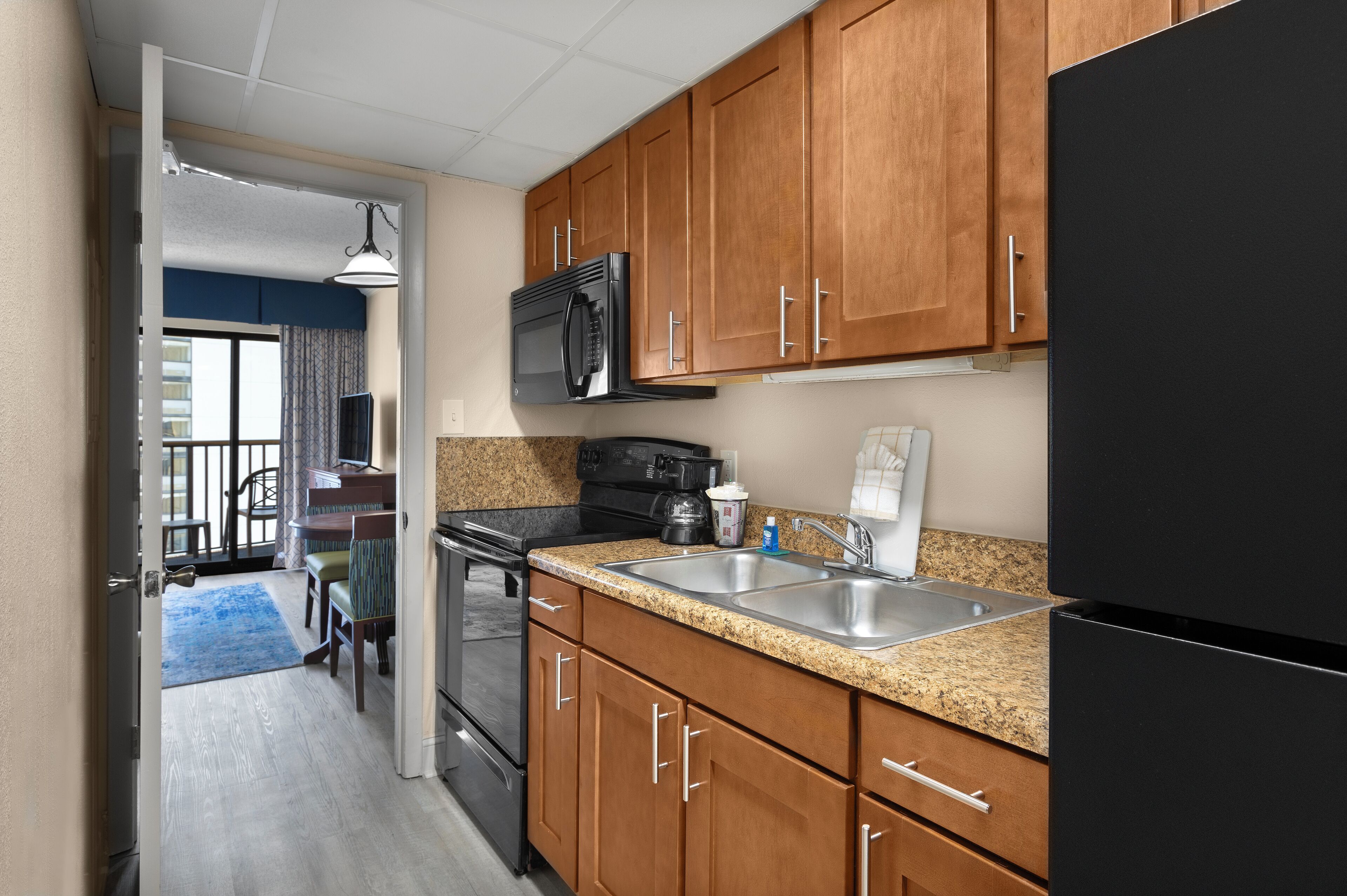 A kitchen with wooden cabinets, a black refrigerator, a stainless steel sink, and a microwave.