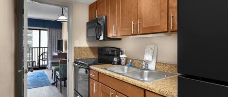 A kitchen with wooden cabinets, a black refrigerator, a stainless steel sink, and a microwave.