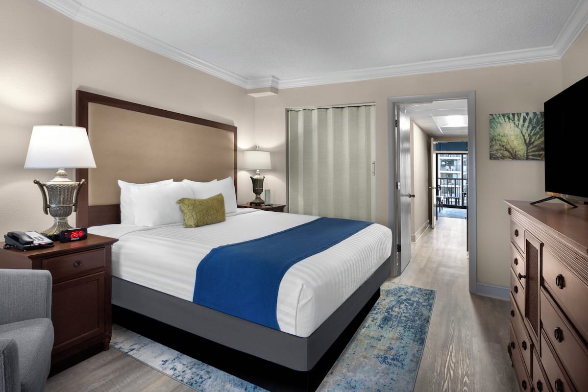 A hotel room with a large bed, bedside lamps, a desk with a telephone, a chair, a dresser, and a television.