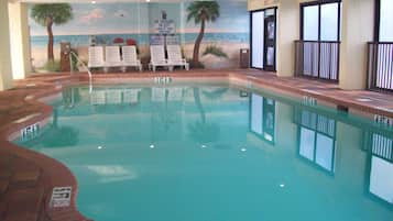 Une piscine intérieure avec des chaises longues, une fresque représentant une scène de plage et un panneau indiquant la présence d’un sauveteur.