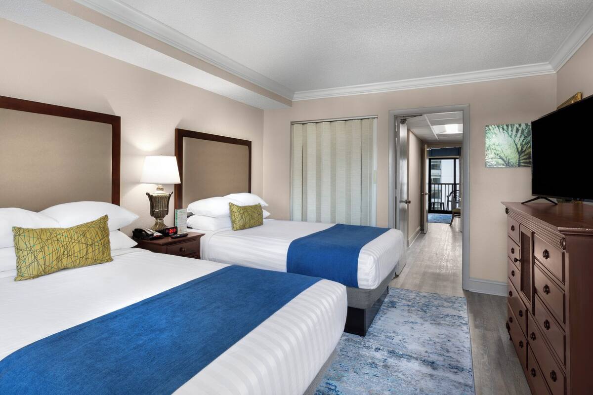 A hotel room with two beds, a TV, a dresser, and a bathroom visible through an open door.