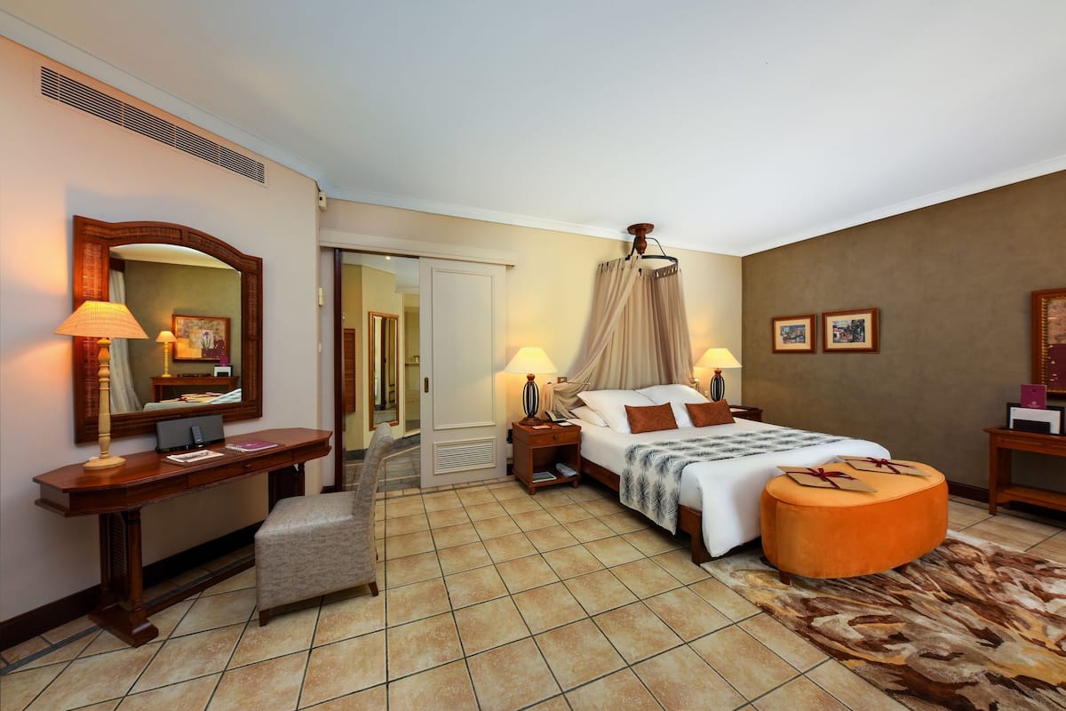 A hotel room with a bed, bedside tables, a desk, a chair, a mirror, and a door leading to another room.
