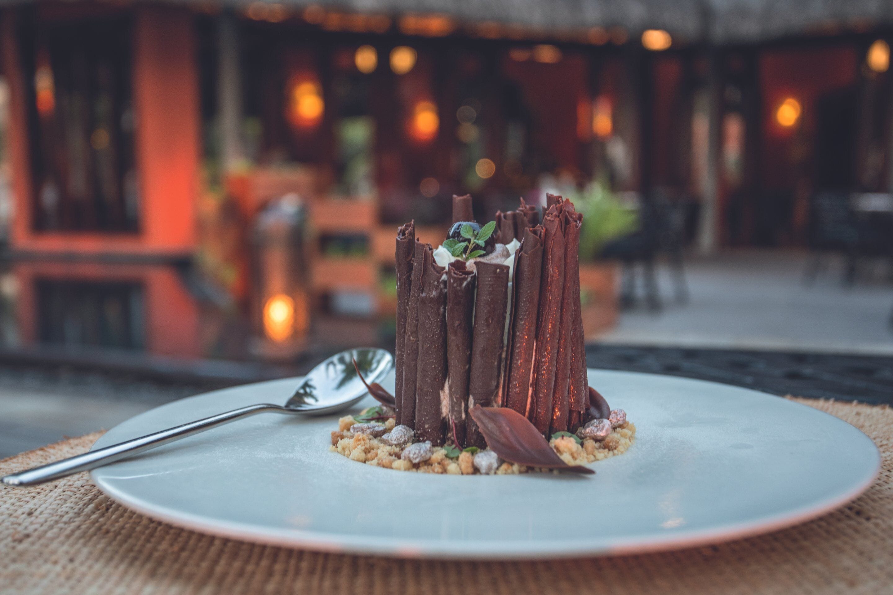 A dessert on a plate with a spoon beside it, set on a table with a woven placemat.