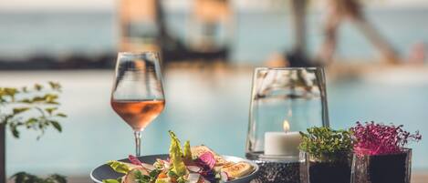 A dining table with a bowl of salad, a glass of wine, a candle, and two small vases with plants.