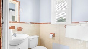 A bathroom with a white sink, toilet, and a window with blinds. - Horse Cave Motel (Horse Cave)