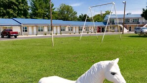 A white horse statue on a concrete base in a grassy area with a building in the background. - Horse Cave Motel (Horse Cave)