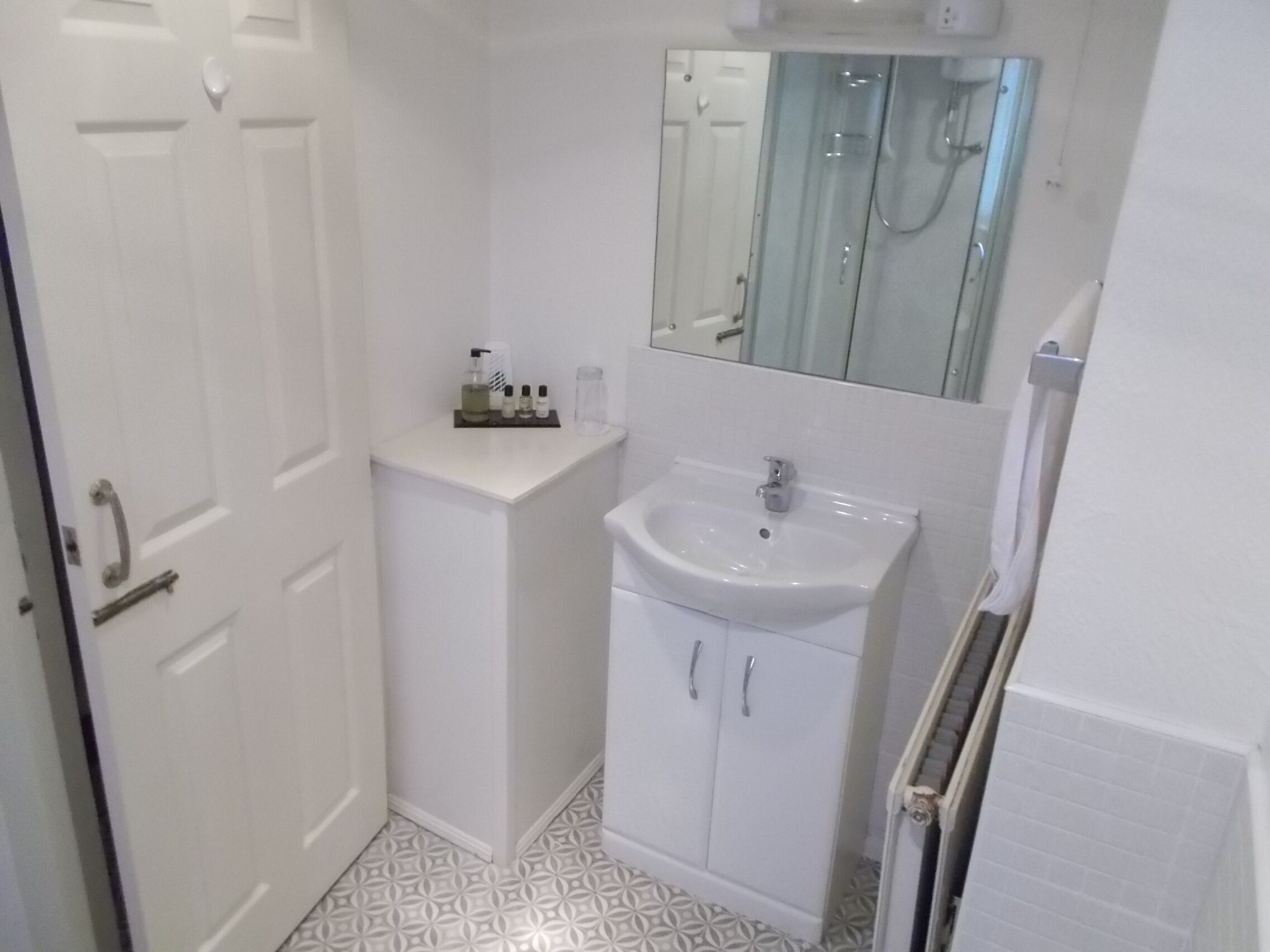 A small, white bathroom with a sink, mirror, and a cabinet with toiletries.