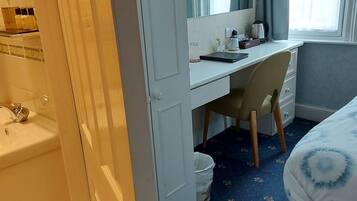 A hotel room with a bed, a desk, a chair, a sink, and a window with curtains.