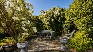 Eine Terrasse mit Tisch und Stühlen, umgeben von üppiger Bepflanzung und blühenden Pflanzen.
