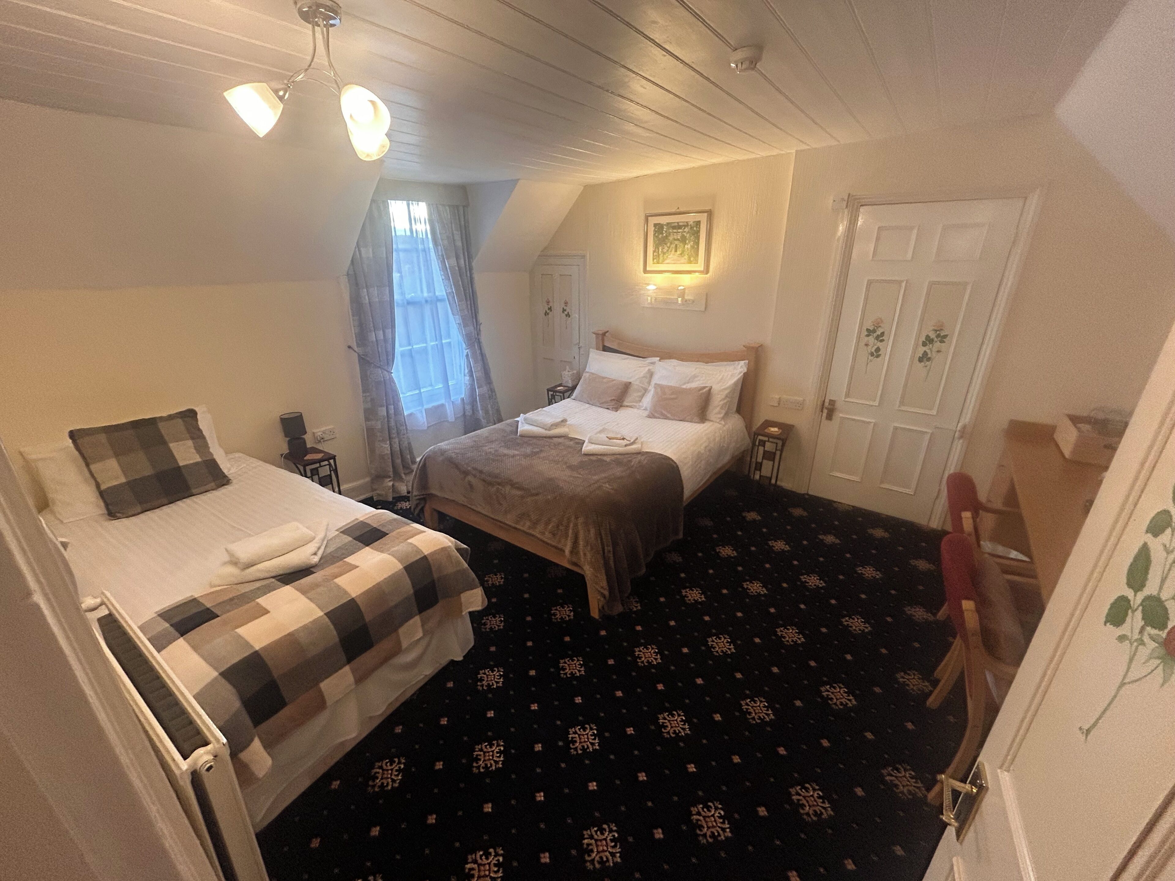 Een slaapkamer met twee bedden, een plafondventilator, een raam met gordijnen, een deur en een kleine tafel.