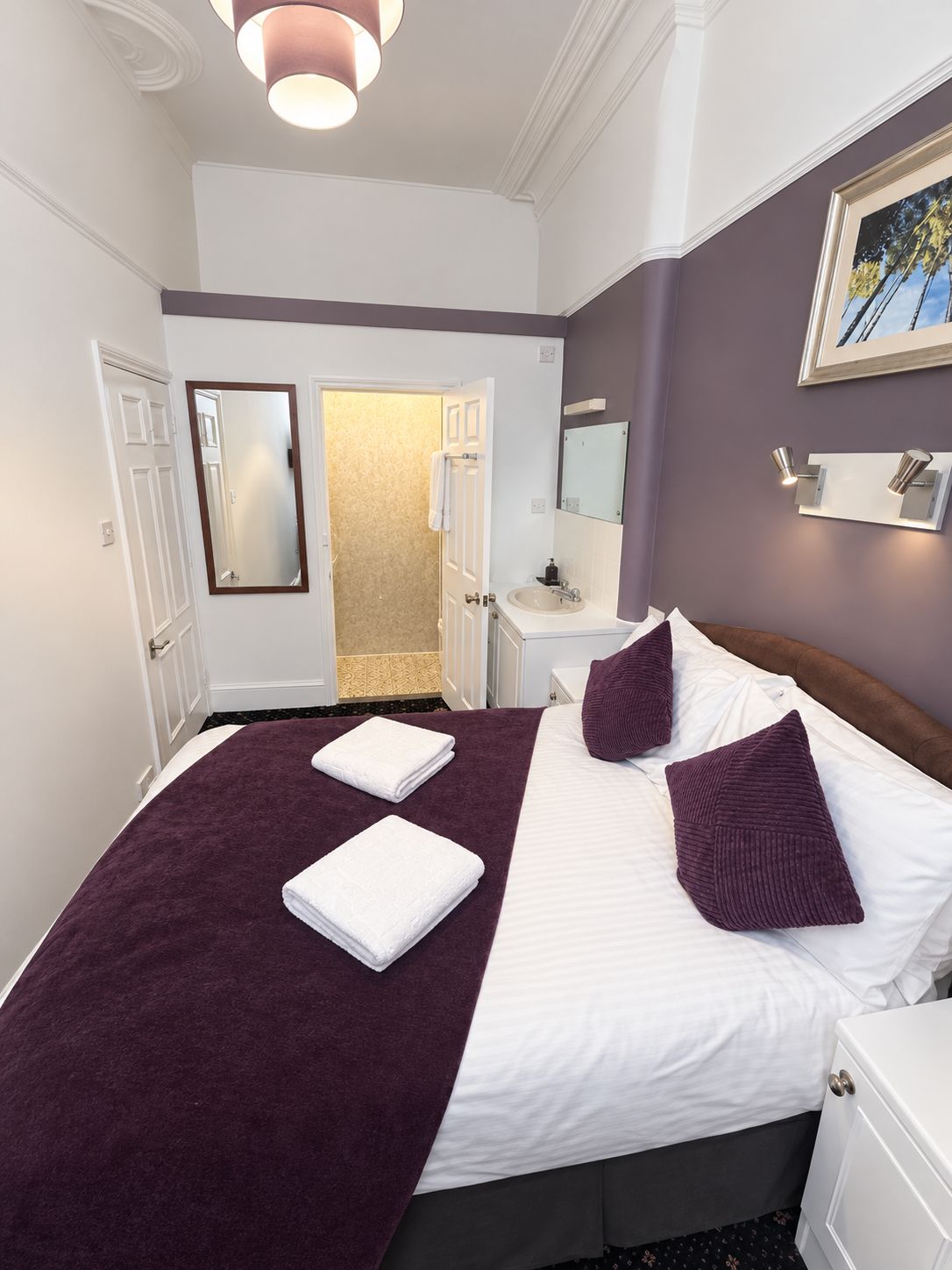 Ein Hotelzimmer mit einem großen Bett, einem Nachttisch, einem Spiegel und einer Tür zu einem Badezimmer.