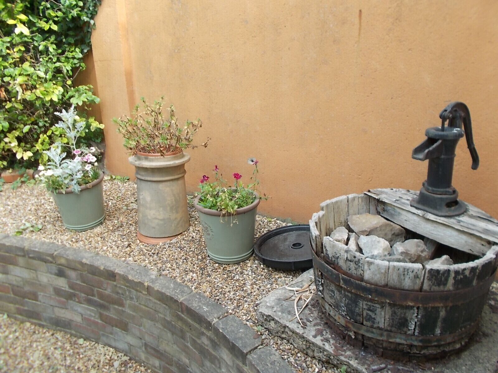 Un giardino con tre piante in vaso e un braciere rustico.