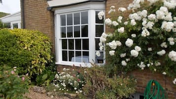 Una casa de ladrillo con un ventanal blanco y un jardín con diversas plantas y flores.